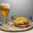 Amber beer in a beer glass next to a clear bowl of rippled chips